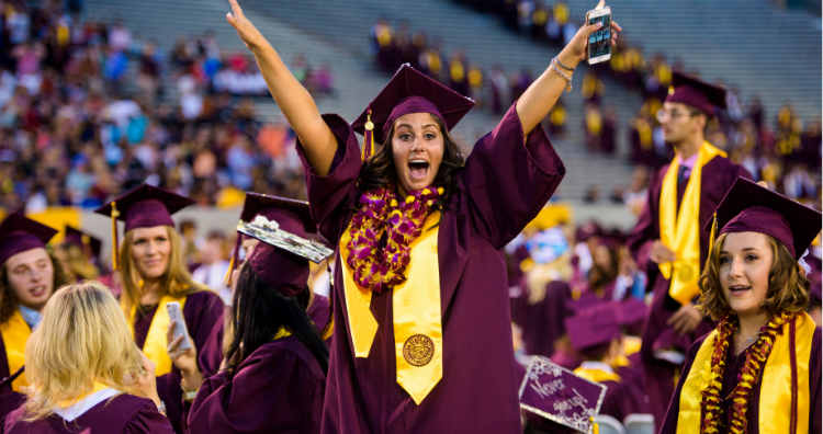 At graduation, an ASU student celebrates in her cap and gown with her arms up high.